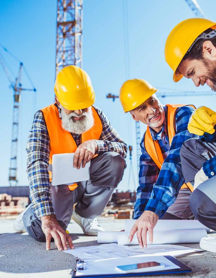 Three construction workers sitting on concrete at construction site, discussing building plans